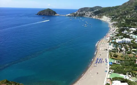Vista panoramica della spiaggia dei Maronti, con il mare blu intenso, tante barche e la costa verdeggiante.