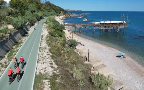 Ciclisti sulla pista ciclabile lungo mare, con i trabocchi che caratterizzano la costa dei Trabocchi cosa vedere. Spiaggia di ciottoli e mare azzurro.