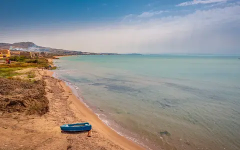 Spiaggia di Licata con barca blu e mare calmo. Un paesaggio da esplorare, tra terra e acqua cristallina.