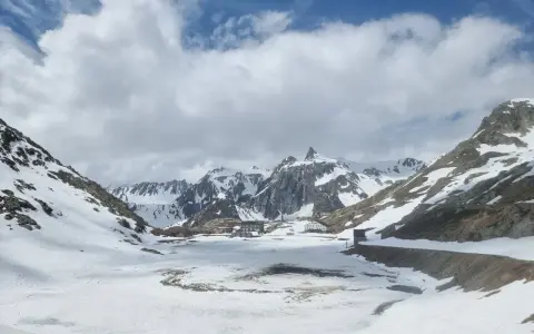 Paesaggio innevato al Gran San Bernardo con edifici storici e montagne maestose sotto un cielo nuvoloso.