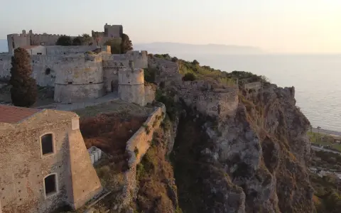 Il complesso monumentale del castello di Milazzo si erge su una scogliera a picco sul mare, con torri e mura antiche che dominano il paesaggio.