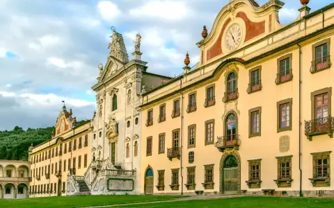 La maestosa Certosa di Calci, con la sua facciata imponente e il prato verde antistante, incanta sotto un cielo nuvoloso.