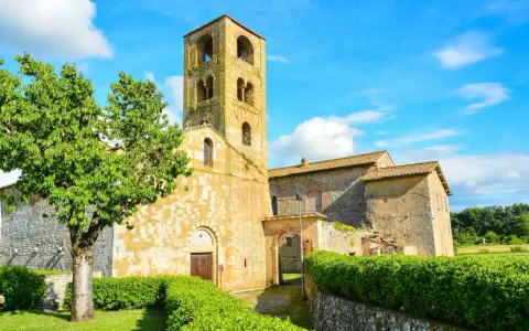Antico campanile romanico e edifici in pietra nel **Sovicille centro storico**, con un albero verdeggiante e cielo azzurro.