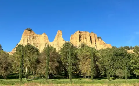 Le maestose balze del Valdarno si ergono sotto un cielo azzurro, circondate da una rigogliosa vegetazione e cipressi slanciati.