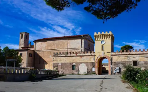 Antico borgo sull'isola di Pianosa, con torre dell'orologio e campanile sotto un cielo azzurro.