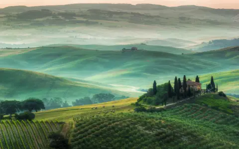 Dolci colline verdi del Val d'Orcia, con una casa colonica in cima a una collina e cipressi. Un paesaggio da cartolina, uno dei tanti punti panoramici mozzafiato.