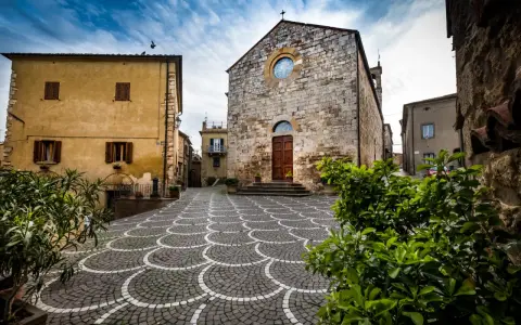 Piazza di Bibbona, cosa vedere: chiesa in pietra con rosone, case gialle e pavimentazione a ventaglio.
