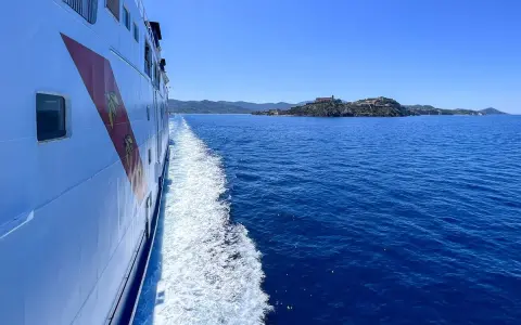 Traghetto in navigazione verso l'isola d'Elba, con la costa all'orizzonte sotto un cielo azzurro.