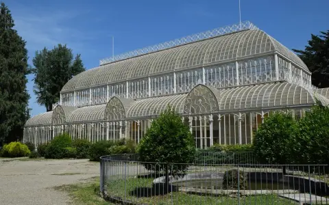 Serra in vetro con archi decorati, parte del giardino orticoltura firenze, circondata da alberi e vegetazione.