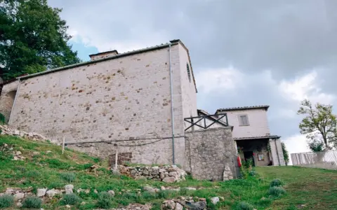 Antico eremo di Cerbaiolo, con muri in pietra grezza e vegetazione rigogliosa che sale sul pendio.