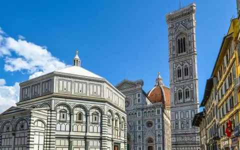 La piazza del Duomo a Firenze con il Battistero, il Campanile di Giotto e la cupola del Brunelleschi sotto un cielo azzurro.