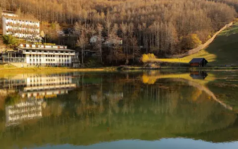 Hotel Cristallo sul Passo del Cerreto, riflesso sull'acqua calma di un lago circondato da boschi autunnali.
