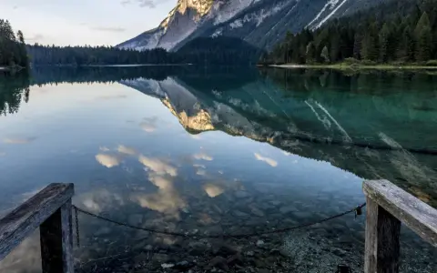 Lago alpino con riflessi di montagne e nuvole, un pontile in legno invita a contemplare la bellezza del Val di Non.