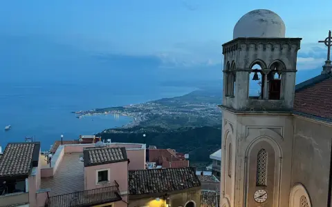 Castelmola cosa vedere: vista panoramica sul mare e sulla costa siciliana, con un campanile in primo piano.