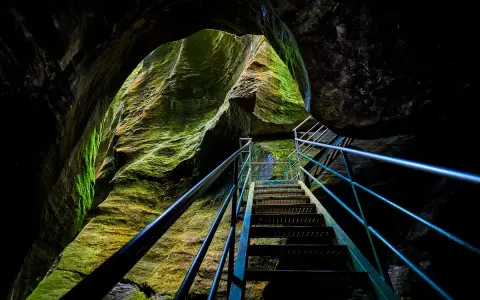 Una scala metallica sale tra le rocce muschiose degli orridi di Uriezzo, illuminata da una luce che filtra dall'alto.