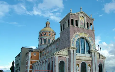 Imponente Santuario di Tindari con cupola dorata e facciata decorata, sotto un cielo azzurro con nuvole bianche.