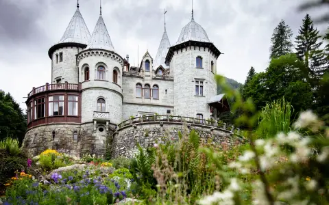 Un fiabesco castello in pietra, tra i castelli Val d'Aosta, circondato da un giardino fiorito e boschi rigogliosi.