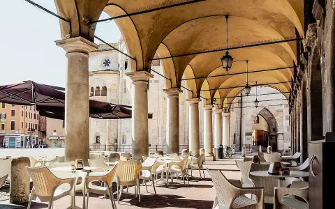 Tavolini all'aperto sotto un portico con vista sul Duomo. Un'idea su cosa fare a Modena: godersi un caffè in piazza.