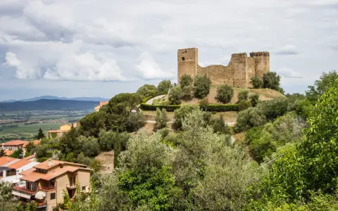 Rovine di un castello dominano il **Scarlino centro storico**, circondato da ulivi e case con tetti rossi.