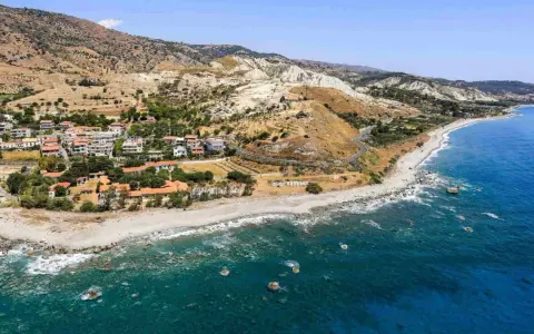 Paesaggio mozzafiato sulla costa ionica Calabria: case con tetti rossi, spiaggia rocciosa e mare blu intenso.