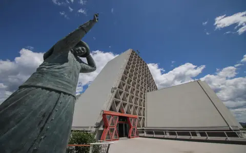 Statua bronzea davanti al Santuario Monte Grisa, con il suo ingresso rosso e la facciata a triangoli.
