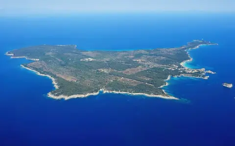 Vista aerea di un'isola verdeggiante, un'isola vicino all'Elba, con acque blu intenso e una piccola isola rocciosa in lontananza.
