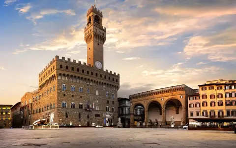 Il maestoso Palazzo Vecchio domina Piazza della Signoria, con la sua torre imponente che svetta sotto un cielo al tramonto.