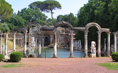 Resti archeologici di Villa Adriana con statue classiche e un laghetto, immersi nel verde.