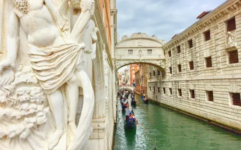 Gondole scivolano sul canale sotto il Ponte dei Sospiri, con un'imponente statua in primo piano.