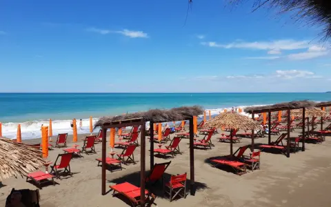 Spiaggia attrezzata a Marina di Bibbona, con lettini rossi, ombrelloni di paglia e il mare azzurro all'orizzonte.