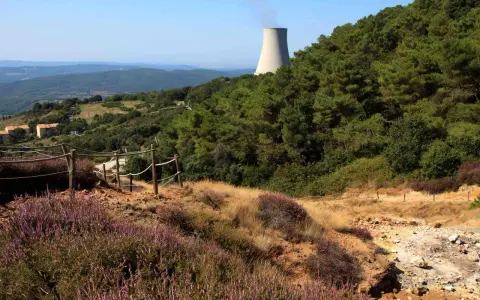 Sentiero nel parco delle Biancane con torretta di raffreddamento in lontananza, circondato da vegetazione e colline.