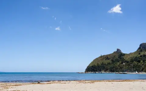 Spiaggia del Poetto con mare azzurro, montagne verdi e un porto turistico pieno di barche.
