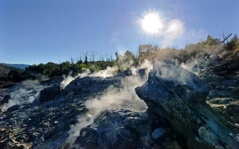 Fumarole attive nel **Val di Cecina**, con vapore che sale tra le rocce sotto un sole splendente.