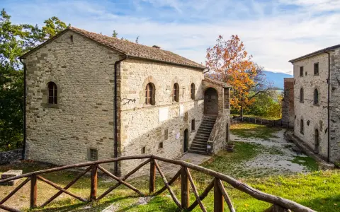 Antica strada in Casentino conduce a un borgo in pietra con un cortile interno e un albero dalle foglie arancioni.