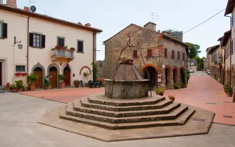 Piazza con pozzo antico a Civitella in Val di Chiana, circondata da case in pietra e intonaco, con fiori colorati.