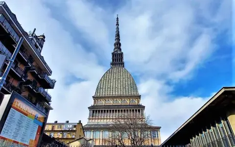 La Mole Antonelliana svetta maestosa nel cielo azzurro di Torino, circondata da edifici moderni e storici.