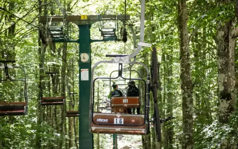 La funivia Monte Amiata trasporta due persone e una mountain bike tra gli alberi rigogliosi.