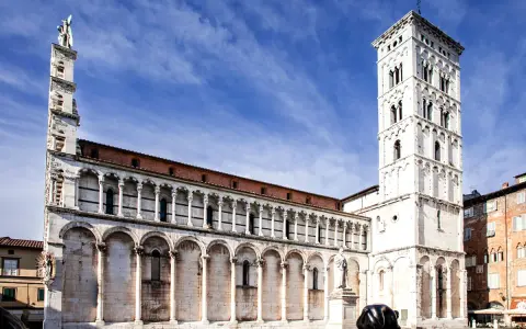 La piazza San Michele a Lucca, con la sua chiesa romanica e la torre campanaria imponente, sotto un cielo azzurro.