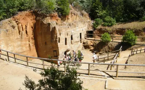 Antiche cave di tufo scavate nella roccia, con finestre e ingressi. Un gruppo di turisti esplora questo luogo affascinante, tra i **baratti cosa vedere** e la natura rigogliosa.