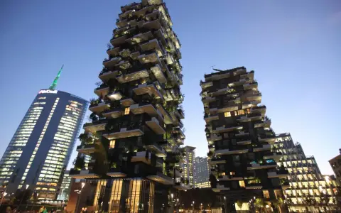 Il Bosco Verticale di Milano, con i suoi grattacieli ricoperti di alberi e piante, si staglia contro il cielo serale.