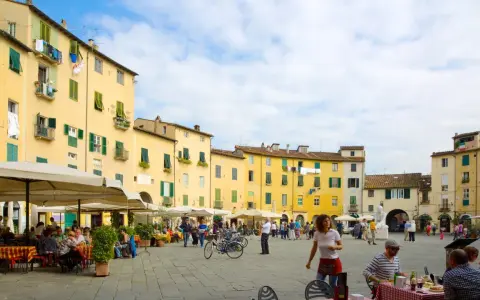 Passeggiata nella storica piazza anfiteatro di Lucca, con i suoi palazzi gialli e i tavolini all'aperto.