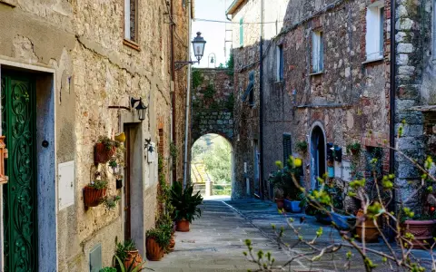 Un vicolo suggestivo a Monteverdi Marittimo, con case in pietra, piante in vaso e un arco che si apre su un paesaggio verde.