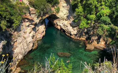 Bagni Regina Giovanna: una baia nascosta con acque cristalline, rocce scolpite e vegetazione lussureggiante. Persone si godono il sole e nuotano.