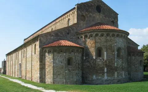 Antica basilica romanica di San Piero a Grado, con absidi semicircolari e tetto in cotto, immersa nel verde.