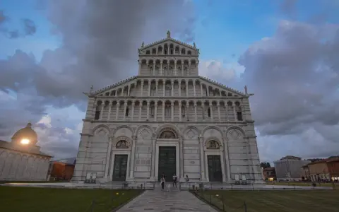 La maestosa **cathédrale de Pise** si erge sotto un cielo nuvoloso, con la sua facciata ricca di arcate e decorazioni.