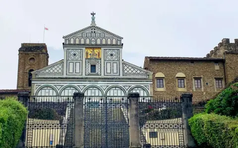 La facciata marmorea di San Miniato al Monte domina la vista, con un cancello in ferro battuto che precede la scalinata.