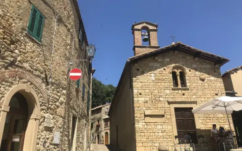 Un vicolo a Casale Marittimo, Pisa, con edifici in pietra, una chiesa con campanile e un tavolino all'aperto.