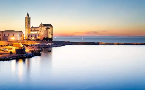 La cattedrale di Trani si erge maestosa sul mare al tramonto, illuminata da luci calde.