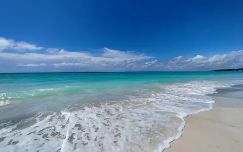 Onde turchesi lambiscono le spiagge bianche di Marina di Cecina, sotto un cielo azzurro con nuvole sparse.