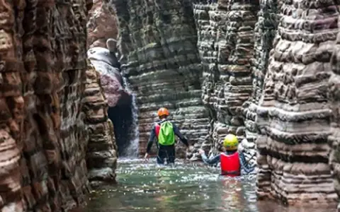 Esploratori in un canyon, tra rocce stratificate e acqua limpida, attraversano i **stretti di giaredo**.